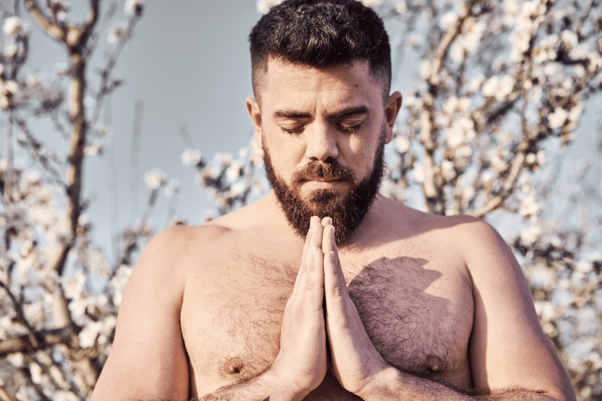 Schwule und Religion. Symbolbild: Mann mit freiem Oberkörper hat die Augen geschlossen und die Hände zum Gebet gefaltet. Englisch: Gay and religious. Symbolic image: Man with bare upper body, eyes closed and hands folded in prayer.