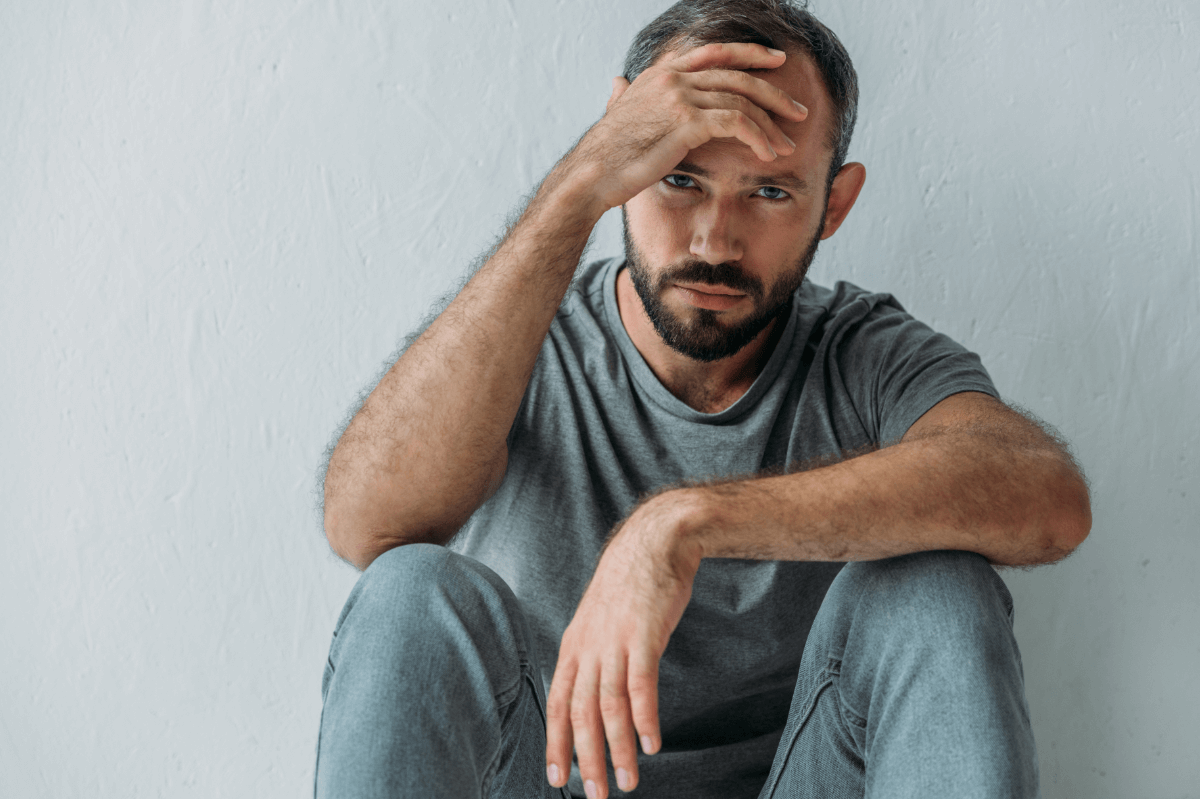 Sucht: Wie Abhängigkeit dein Leben beeinflusst. Symbolbild: Ein Mann sitzt niedergeschlagen da und hält sich die Stirn. Addiction: How addiction can change your life. symbolic image: a man sitting with his hand on his forehead
