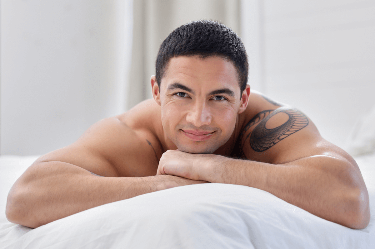 Prostata Massage Symbolbild: Ein Mann mit freiem Oberkörper liegt auf dem Bauch und lächelt in die Kamera. Englisch: Prostate massage, symbolic image: a naked man is lying on his front smiling at the camera.