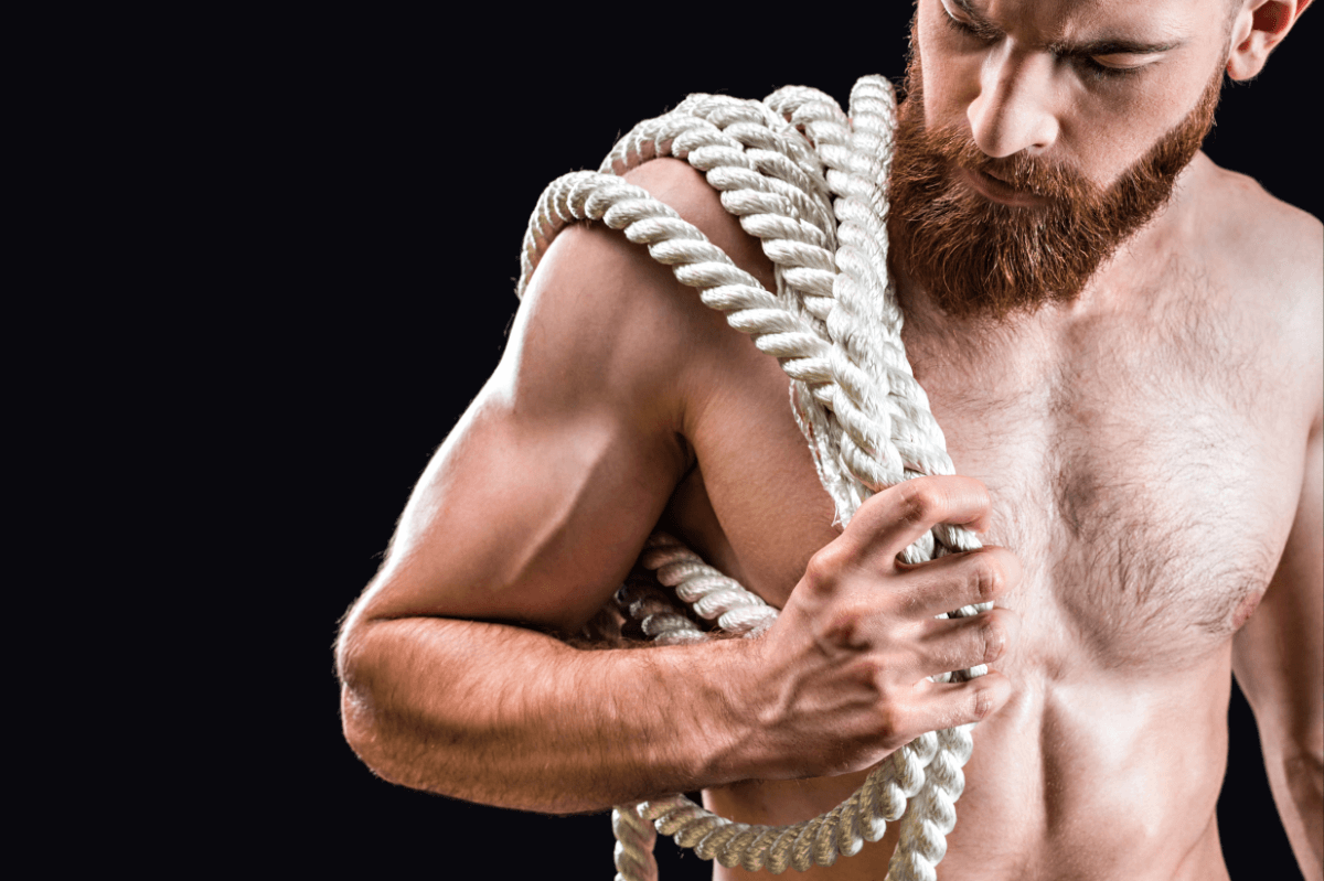 Rigger BDSM oder Rope Top. Symbolbild: Ein Mann mit freiem Oberkörper trägt ein dickes Seil. Englisch: Rigger or rope top. Symbolic image: a shirtless man carries a thick rope.
