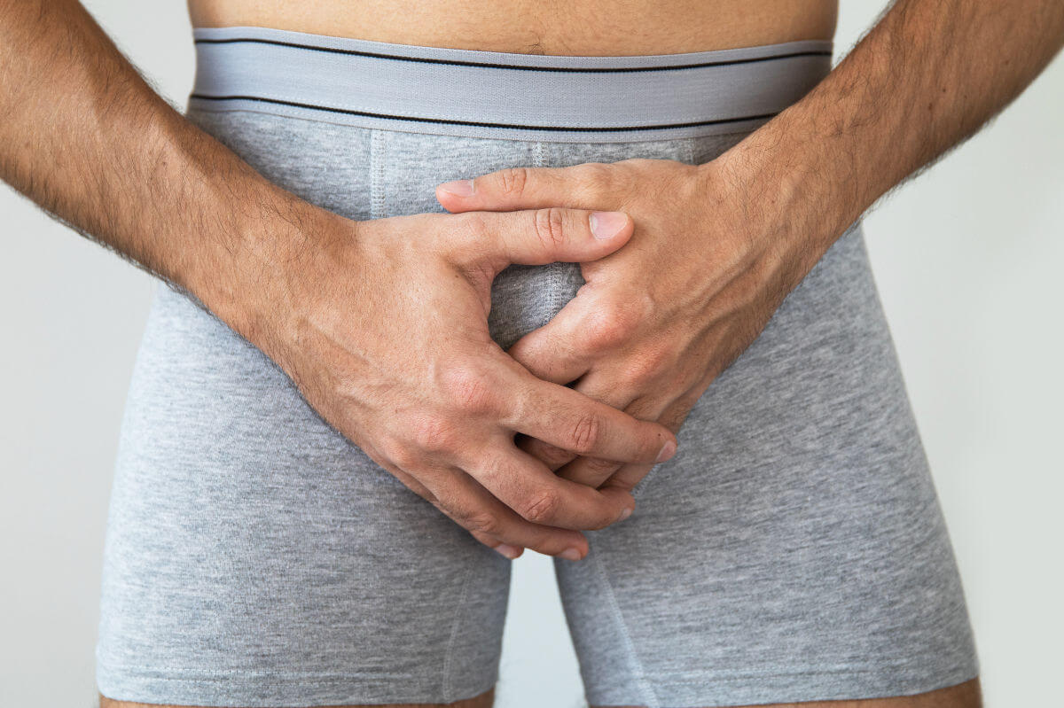 Beschneidung Symbolbild: Bildausschnitt eines männlichen Genitalbereichs in Unterhose, bei dem die Hände vor das Geschlechtsteil gelegt sind. Englisch: Circumcision Symbolic image: detail of a male genital area in underpants, with the hands placed in front of the genitals.