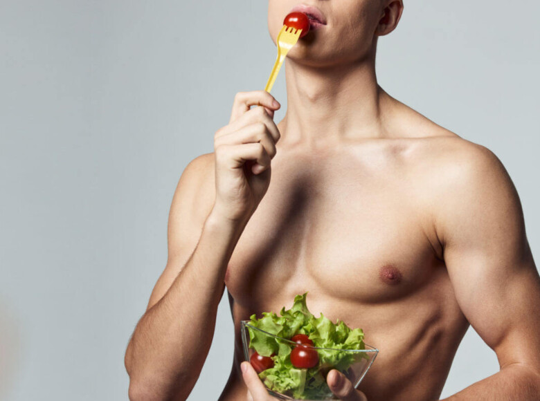 Analsex Vorbereitung Symbolbild: Ein männlicher nackter Oberkörper hält einen Salat in den Händen und führt eine Tomate auf der Gabel zum Mund. Anal sex preparation Symbolic image: A naked male torso holds a salad in his hands and brings a tomato on a fork to his mouth.