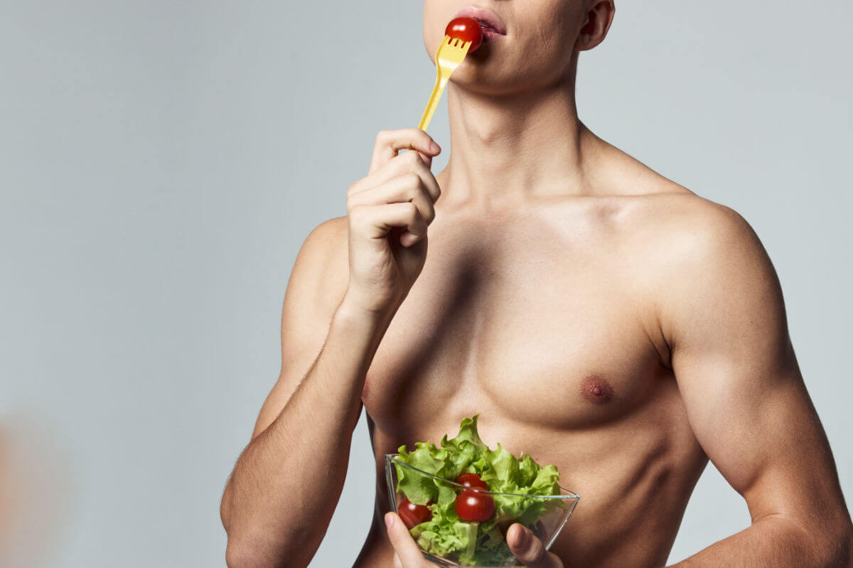 Analsex Vorbereitung Symbolbild: Ein männlicher nackter Oberkörper hält einen Salat in den Händen und führt eine Tomate auf der Gabel zum Mund. Anal sex preparation Symbolic image: A naked male torso holds a salad in his hands and brings a tomato on a fork to his mouth.