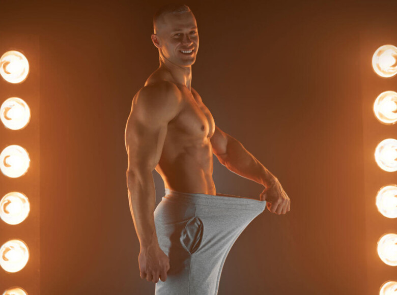 Penislänge Symbolbild: Ein Mann mit nacktem Oberkörper hält seine Hose im Schritt soweit von sich weg, dass ein langer Penis angedeutet wird. Englisch: Penis length Symbolic image: A man with a bare upper body holds his pants away from his crotch, suggesting a long penis.