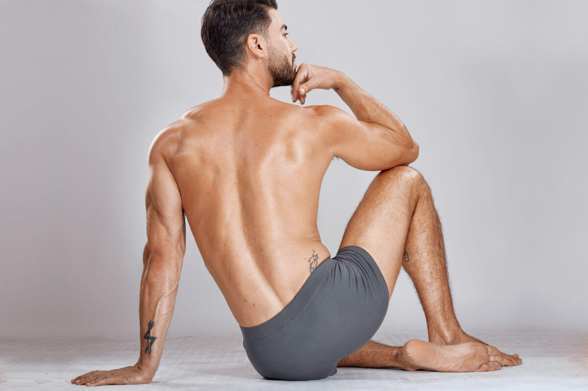 Prostatamassage Symbolbild: Ein Mann, nur mit Unterhose bekleidet, sitzt mit dem Rücken zur Kamera auf dem Boden. Englisch: Prostate massage Symbolic image: A man wearing only underwear is sitting on the floor with his back to the camera.