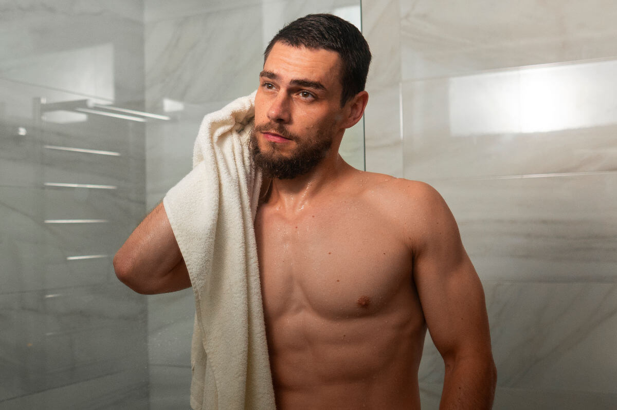 Analsex Reinigung Symbolbild: ein Mann kommt aus der Dusche und trocknet sich mit dem Handtuch ab. Englisch: Anal sex cleaning Symbolic image: a man comes out of the shower and dries himself with a towel.