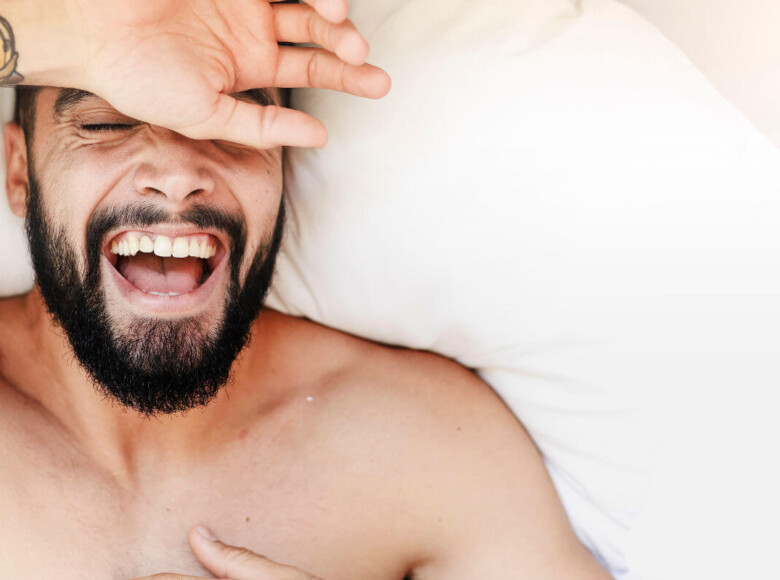 Ist Masturbieren gesund? Symbolbild: Gesicht eines Mannes, der sehr glücklich im Bett liegt. Is masturbation healthy? Symbolic image: Face of a man lying very happily in bed.