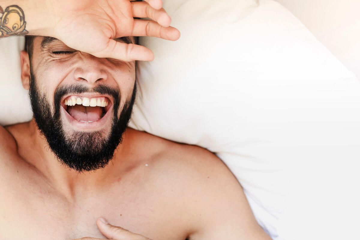 Ist Masturbieren gesund? Symbolbild: Gesicht eines Mannes, der sehr glücklich im Bett liegt. Is masturbation healthy? Symbolic image: Face of a man lying very happily in bed.