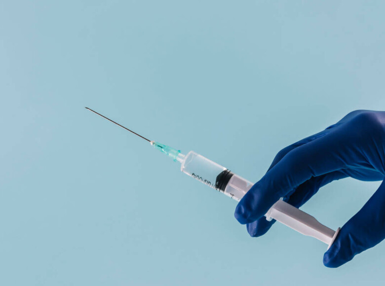 Spritze in den Penis. Symbolbild: Eine Hand mit medizinischem Handschuh hält eine Spritze. Englisch: Penis Injection. Symbolic image: A hand wearing a medical glove holding a syringe.