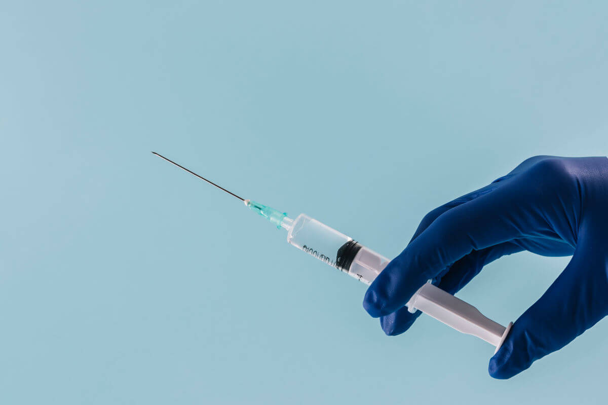 Spritze in den Penis. Symbolbild: Eine Hand mit medizinischem Handschuh hält eine Spritze. Englisch: Penis Injection. Symbolic image: A hand wearing a medical glove holding a syringe.