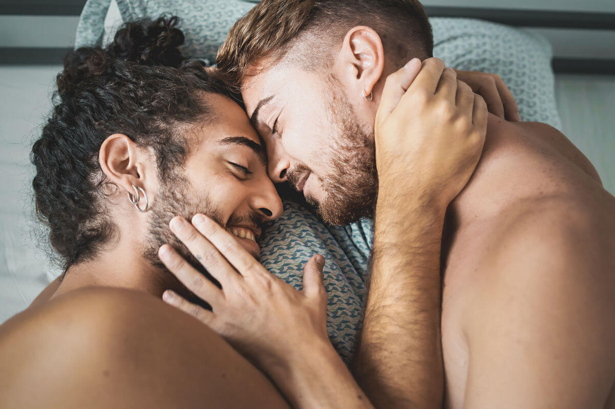 Frotting vs. Dry Humping Symbolbild: Zwei Männer liegen nackt im Bett und kuscheln. Frotting vs. Dry Humping Symbolic image: Two men lying naked in bed and cuddling.