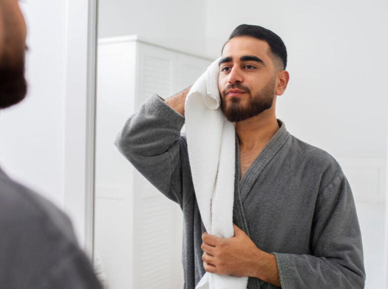 BDSM-Aftercare Symbolbild: Ein Mann mit Bademantel bekleidet trocknet sich nach dem Duschen das Gesicht mit einem Handtuch ab. . BDSM aftercare Symbolic image: A man wearing a bathrobe dries his face with a towel after showering.