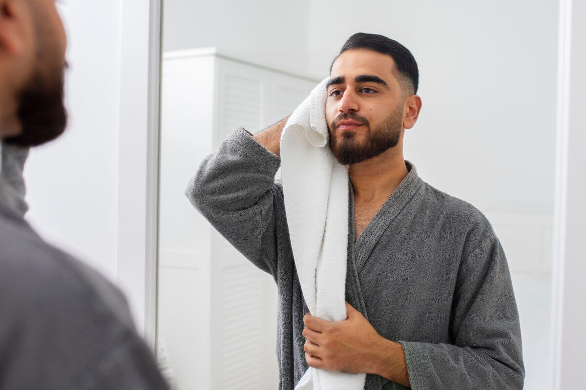 BDSM-Aftercare Symbolbild: Ein Mann mit Bademantel bekleidet trocknet sich nach dem Duschen das Gesicht mit einem Handtuch ab. . BDSM aftercare Symbolic image: A man wearing a bathrobe dries his face with a towel after showering.