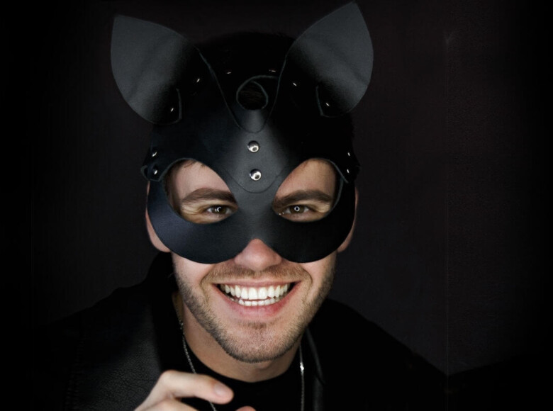 Kittenplay Symbolbild: Mann mit schwarzer Katzenmaske lächelt in die Kamera. . Kitten play Symbolic image: Man wearing a black cat mask smiles at the camera.