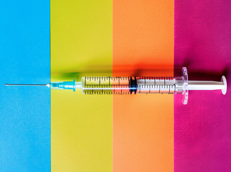 Impfungen für Männer Symbolbild: Eine Spritze liegt auf einem bunt gestreiften Hintergrund. Vaccinations for men Symbolic image: A syringe lies on a colorful striped background.