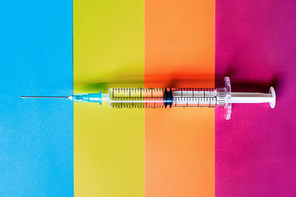 Impfungen für Männer Symbolbild: Eine Spritze liegt auf einem bunt gestreiften Hintergrund. Vaccinations for men Symbolic image: A syringe lies on a colorful striped background.