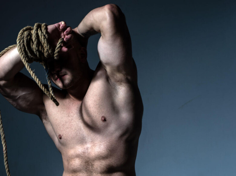 Shibari vs. Kinbaku Symbolbild: Nackter männlicher Oberkörper, das Gesicht wird von einem dicken Seil verdeckt. Englisch: Shibari vs. Kinbaku Symbolic image: Naked male torso, face covered by a thick rope.