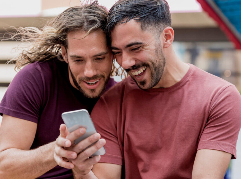 Symbolbild: Zwei Männer schauen gemeinsam auf ein Handy. Symbolic image: Two men looking at a cell phone together.