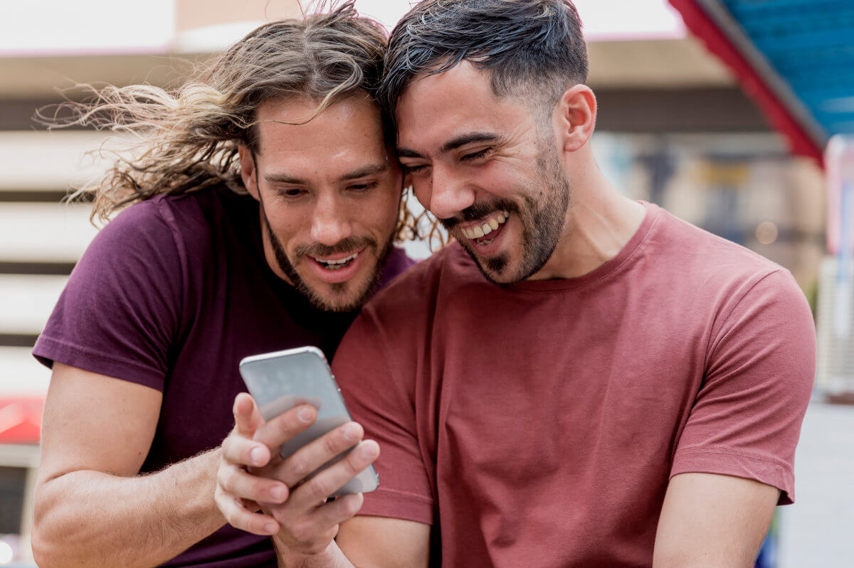 Symbolbild: Zwei Männer schauen gemeinsam auf ein Handy. Symbolic image: Two men looking at a cell phone together.